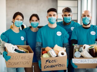 Group of volunteers wearing protective face masks and holding donation boxes while looking at camera.